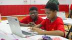 Two young boys in red shirts working on a laptop in a classroom setting.